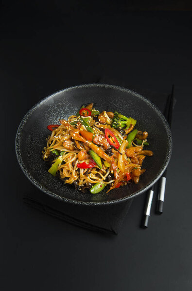 Asian noodles with chicken, vegetables in black bowl and chopsticks. Asian food style