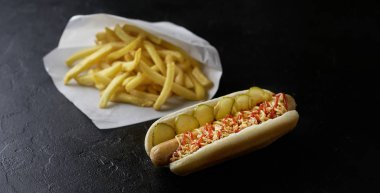 Siyah arka planda patates kızartması olan sosisli sandviç. Fast food konsepti