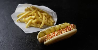 Hot dog with french fries on a black background. Fast food concept clipart