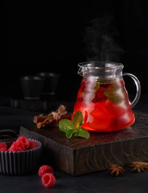 Cam çaydanlıkta ahududu ve ahşap zemin üzerinde nane ile sıcak kırmızı meyve çayı.