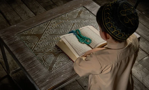 Muchacho musulmán en ropa árabe leyendo el libro sagrado del Corán y orando a Allah, concepto de celebración ramadán niño joven en momento de paz espiritual dentro del interior oriental tradicional — Foto de Stock