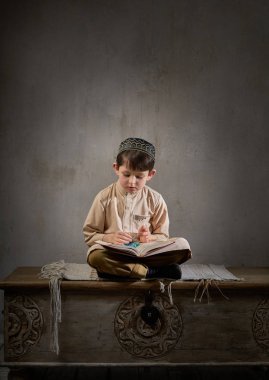 Arap elbiseli, tespih boncuklu küçük müslüman çocuk. Kutsal Kur 'an kitabı okuyor. Allah' a dua ediyor, Ramazan Kareem kavramı.