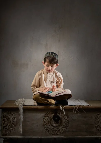 Arap elbiseli, tespih boncuklu küçük müslüman çocuk. Kutsal Kur 'an kitabı okuyor. Allah' a dua ediyor, Ramazan Kareem kavramı.