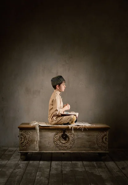 Niño con ropa árabe leyendo libro sagrado quran rezando a Allah, ramadan kareem concepto niño momento espiritual pacífico en el interior oriental tradicional — Foto de Stock
