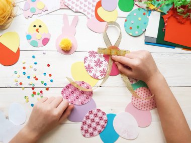 Çocuk Paskalya için kendi elleriyle el sanatları yapıyor. Renkli kağıttan yapılmış renkli bir el yapımı. Makas, karton, yumurta, tavuk, tavşan. Ahşap bir masada sanat yaratıcılığı. Üst görünüm, alanı kopyala