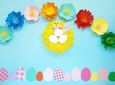 El yapımı yuva, çiçekler farklı renkler, kartondan yapılmış yumurta içindeki tavuk. Mavi arka planda sevimli sanat yaratıcılığı. Paskalya 'da el sanatları reklam konsepti. Düz yat, üst görünüm, kapat, boşluğu kopyala