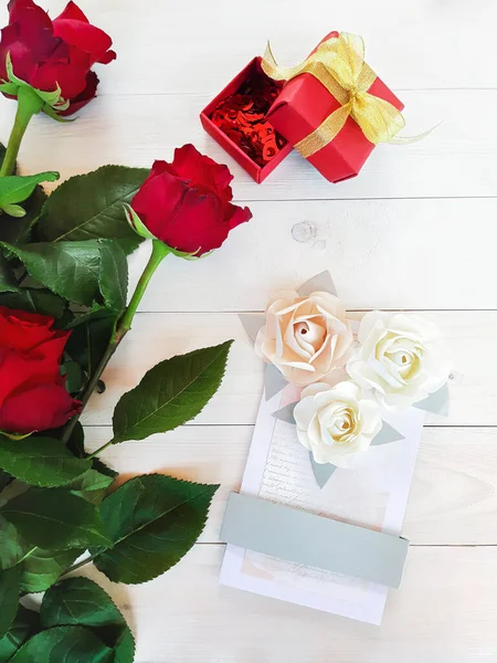Composition of red roses, handmade card with paper roses and gift box with hearts inside on a wooden table. Content for Birthday, Valentines Day, Womens day. Flat lay, top view, close up, copy space