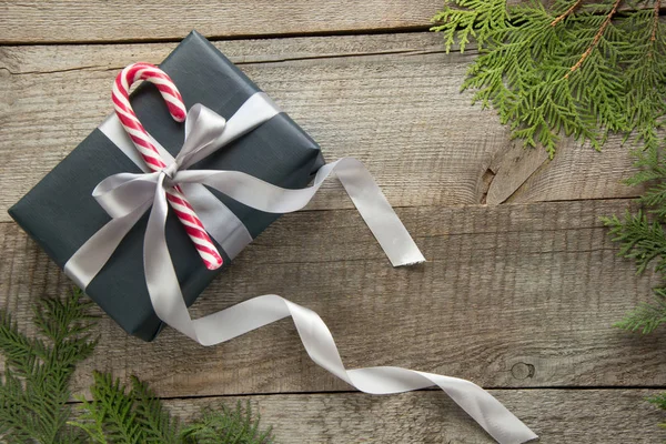 Coffret cadeau de Noël enveloppé dans du papier noir avec des flocons de neige autour du cyprès de branche sur la surface en bois . — Photo