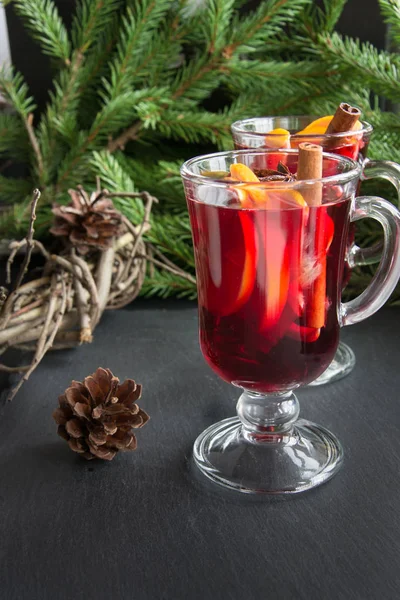 Hot Mulled wijn met kaneel en kerstboom, kegel op zwarte leisteen schotel. — Stockfoto