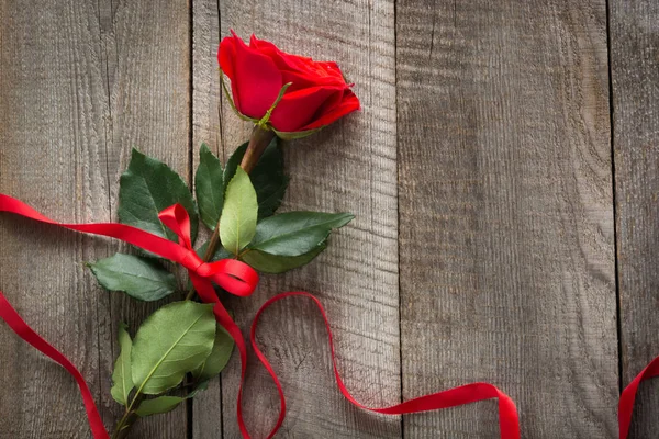 Tarjeta de San Valentín. Rosa roja con cinta sobre tabla de madera. Vista superior . — Foto de Stock