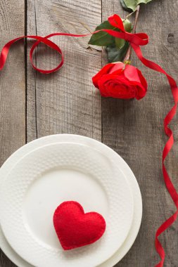 Romantik bir akşam yemeği kavramı. Ahşap arka plan üzerinde Sevgililer günü Festival Tablo ayarı. Plaka üzerinde şerit ve kalp ile kırmızı gül.