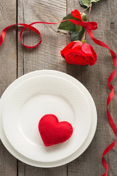 Romantik bir akşam yemeği kavramı. Ahşap arka plan üzerinde Sevgililer günü Festival Tablo ayarı. Plaka üzerinde şerit ve kalp ile kırmızı gül.