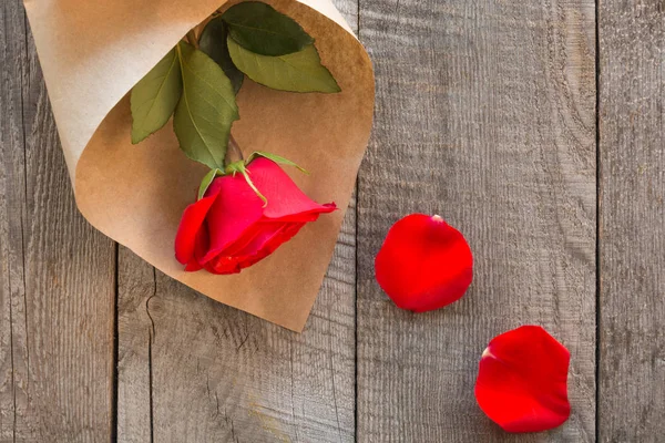 Tarjeta de San Valentín. Rosas rojas envueltas en papel y pétalos sobre fondo de mesa de madera. Vista superior . — Foto de Stock