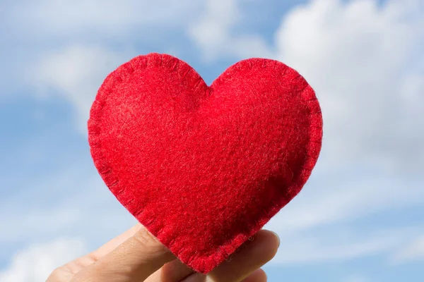Красный чувствовал форму сердца в руке на голубом небе с облаками в качестве фона. Открытки на день святого Валентина . — стоковое фото