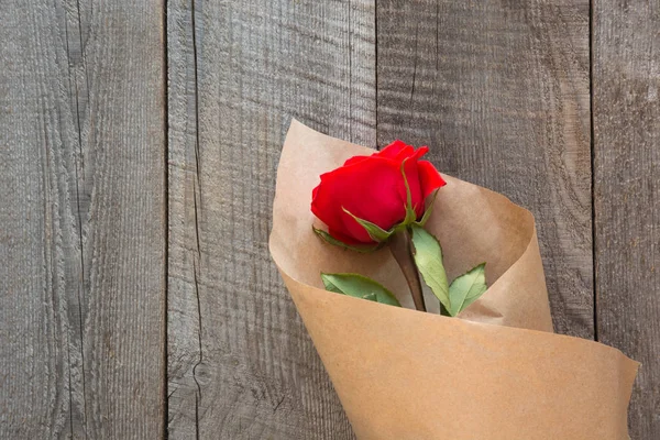 Tarjeta de San Valentín. Rosas rojas envueltas en papel sobre fondo de mesa de madera. Vista superior . — Foto de Stock