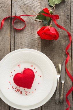 Romantik bir akşam yemeği kavramı. Ahşap arka plan üzerinde Sevgililer günü Festival Tablo ayarı. Plaka üzerinde şerit ve kalp ile kırmızı gül.