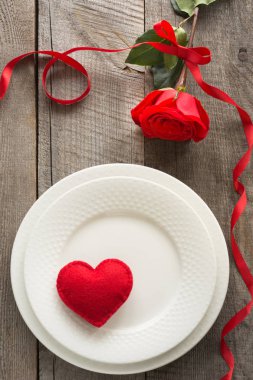 Romantik bir akşam yemeği kavramı. Ahşap arka plan üzerinde Sevgililer günü Festival Tablo ayarı. Plaka üzerinde şerit ve kalp ile kırmızı gül.