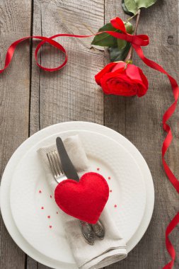 Romantik bir akşam yemeği kavramı. Ahşap arka plan üzerinde Sevgililer günü Festival Tablo ayarı. Plaka üzerinde şerit ve kalp ile kırmızı gül.
