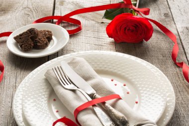 Romantik bir akşam yemeği kavramı. Ahşap arka plan üzerinde Sevgililer günü Festival Tablo ayarı. Kırmızı kurdele ile masaya gül..