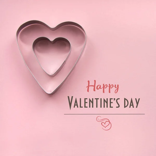 Tarjeta de San Valentín. Un cortador de galletas en forma de corazón dentro de otro sobre fondo rosa con inscripción . — Foto de Stock