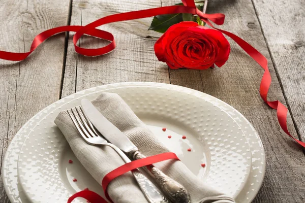 Romantik bir akşam yemeği kavramı. Ahşap arka plan üzerinde Sevgililer günü Festival Tablo ayarı. Kırmızı kurdele ile plaka üzerinde yükseldi..