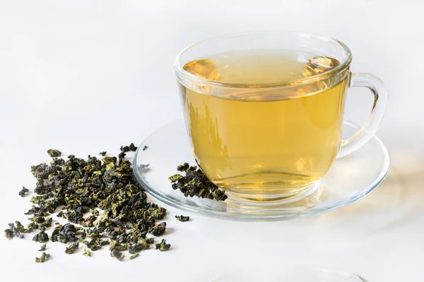 Üveg csésze zöld tea és száraz levelek a zöld tea, fehér háttér. — Stock Fotó