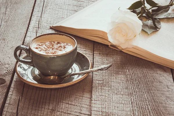 Cup of black coffee and open book with white rose on wooden board. Vintage toned. Close up. — Stock Photo, Image