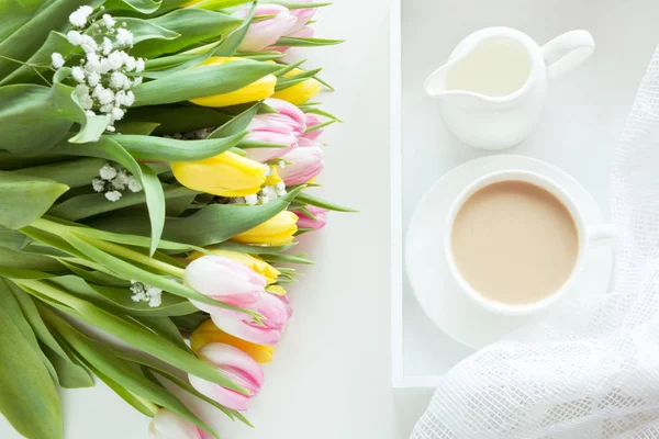 stock image Morning breakfast in spring with a cup of black coffee with milk and pastries in the pastel colors, a bouquet of fresh yellow and pink tulips on a white background. Top view.