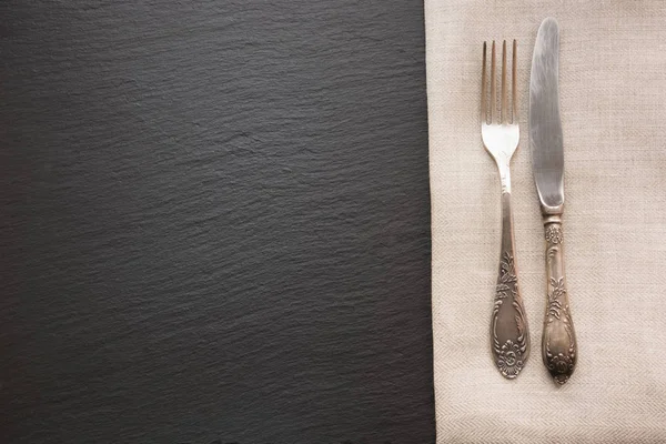 Rustic linen napkin, silverware and black slate dish with copy space for your menu or recipe. Menu card for restaurants.