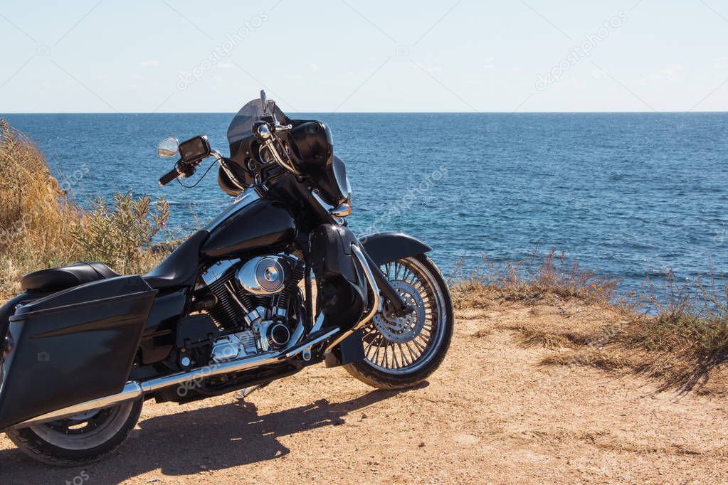 Black motorcycle on beautiful seacoast and blue sky onward. Prairie, steppe, summer.