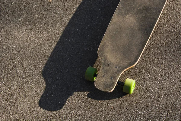 Old used longboard on the asphalt. Old style. Black skateboard on an empty asphalt road. — Stock Photo, Image