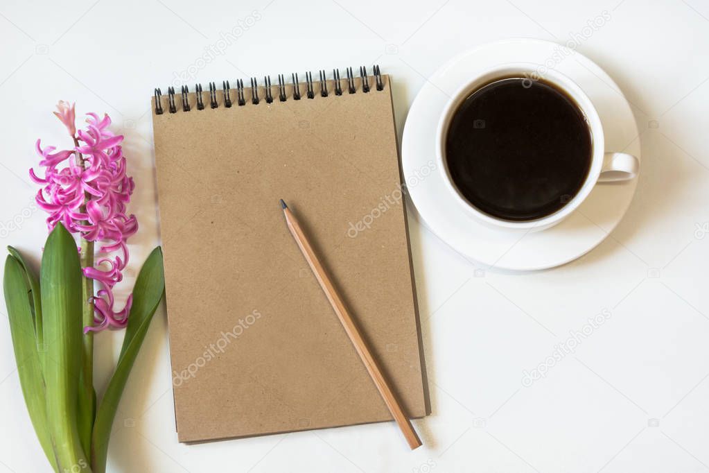 Workspace for blogger with notebook of craft paper, pencil, cup of coffee, flower on white background. Image with copy space for your text.
