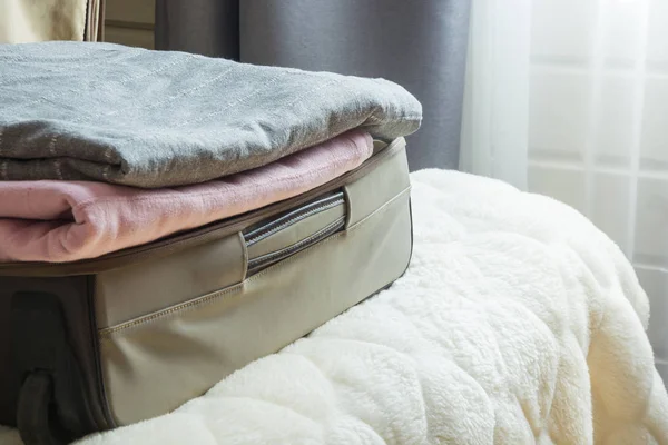 Open door and open suitcase with clothes on the bed.
