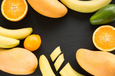 Taze tropikal meyve, mango, muz, portakal, limon, siyah arduvaz çanak üzerinde etrafında avokado. Yukarıdan görüntüleyin. Metin için yer.