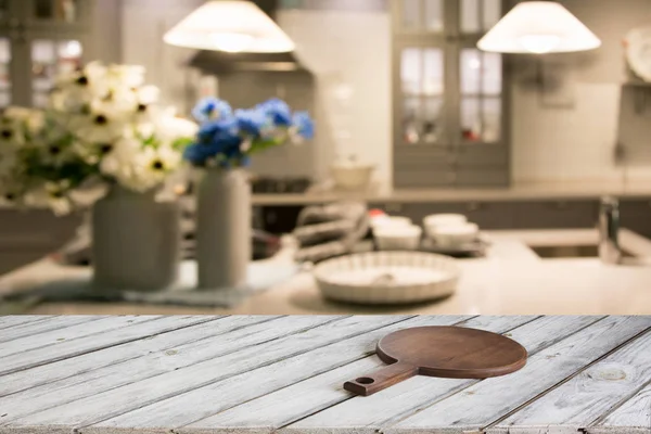 Blurred and abstract kitchen background. Empty wooden tabletop with cutting board  and defocused modern kitchen for display or montage your products.