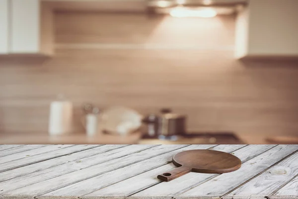 Desfocado e abstrato fundo da cozinha. Mesa de madeira vazia com placa de corte e cozinha moderna desfocada para exibir ou montar seus produtos . — Fotografia de Stock