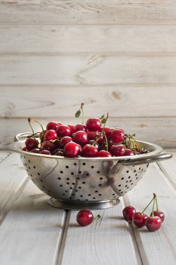 Metal süzgeç veya olgun çilek ve vişne ahşap arka plan üzerine bir kase. Kevgir ile taze kiraz rustik bir tahta üzerinde dolu..