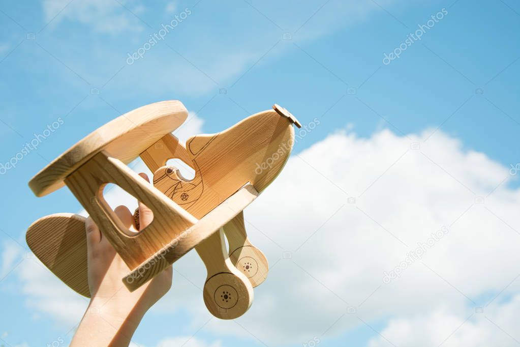 Toy airplane in hand and blue cloudy sky as background.