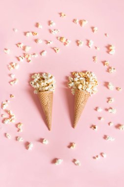 Pembe bir arka plan üzerinde dondurma koni içinde patlamış mısır. Üstten Görünüm.