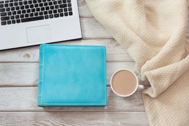 Kadın çalışma alanı ile bir dizüstü bilgisayar, fincan kahve, mavi defter ve hafif ahşap arka plan üzerinde rahat kazak. Kopya alanı ile üstten görünüm kompozisyon.