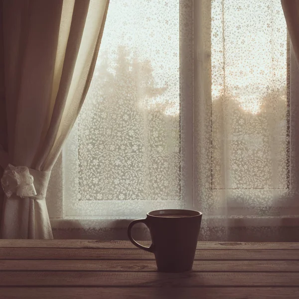 Fincan sade kahve ya da çay ahşap masa üstünde belgili tanımlık pencere önünde. Uzay kopyalayın. Romantik günbatımı.