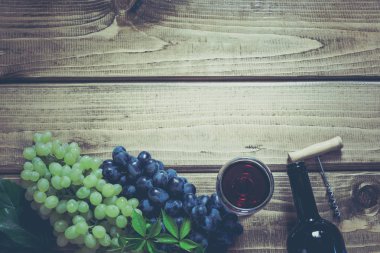 Açık bir şişe kırmızı şarap cam, tirbuşon ve ahşap arka plan üzerinde olgun üzüm ile. Kopya alanı ve üstten görünüm.