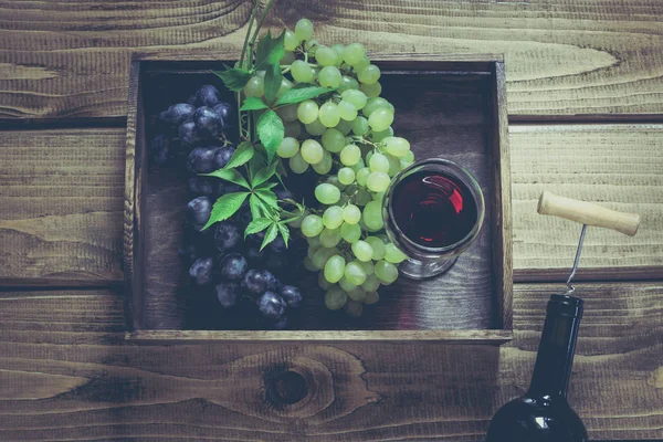 Açık şişe şarap cam, tirbuşon ve olgun üzüm içinde tepsi ahşap arka plan üzerinde. Kopya alanı ve üstten görünüm.