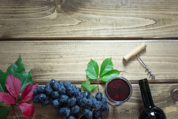 Açık bir şişe kırmızı şarap cam, tirbuşon ve ahşap bir gemide olgun üzüm ile. Kopya alanı ve üstten görünüm.