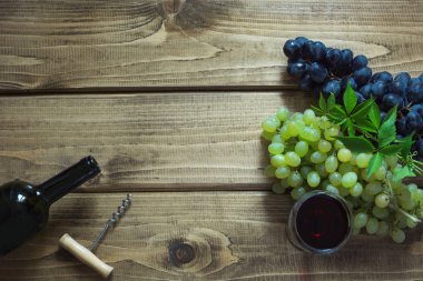 Açık bir şişe kırmızı şarap cam, tirbuşon ve ahşap bir gemide olgun üzüm ile. Kopya alanı ve üstten görünüm.