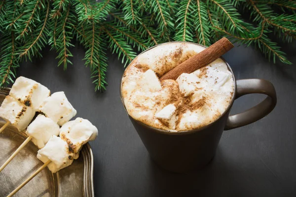 Tradycyjny napój świąteczny. Gorąca czekolada z pianki i cynamon na czarnym tle z gałęzi choinki. Z bliska. — Zdjęcie stockowe