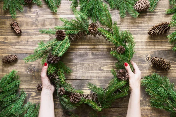 Karácsonyi koszorú a fenyő ágak fából készült táblán a női kéz. Szemközti nézet. — Stock Fotó