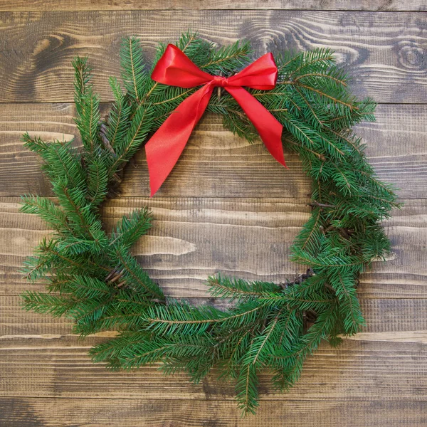 Corona de Navidad con ramas de abeto con lazo rojo sobre tabla de madera. Acostado. Vista superior . — Foto de Stock