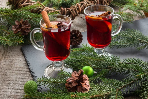 Χριστουγεννιάτικο ζεστό ζεστό κρασί με κανέλα, πορτοκάλι και χριστουγεννιάτικο δέντρο σε μαύρο σχιστόλιθο πιάτο. — Φωτογραφία Αρχείου