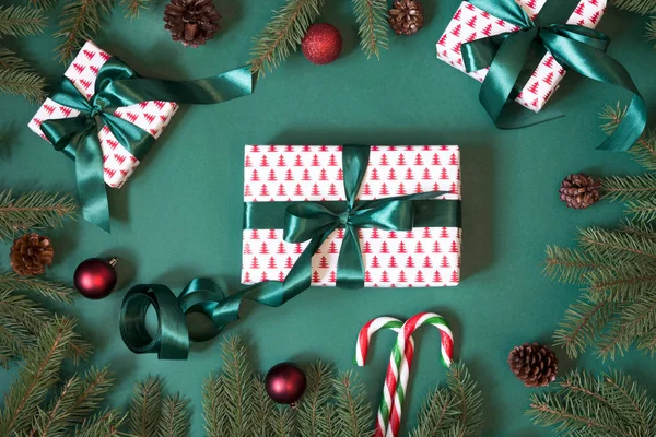 Weihnachtsgeschenkschachteln und Geschenkverpackungen in Designpapier und grünem Band auf Grün mit rotem Dekor. Ansicht von oben. — Stockfoto